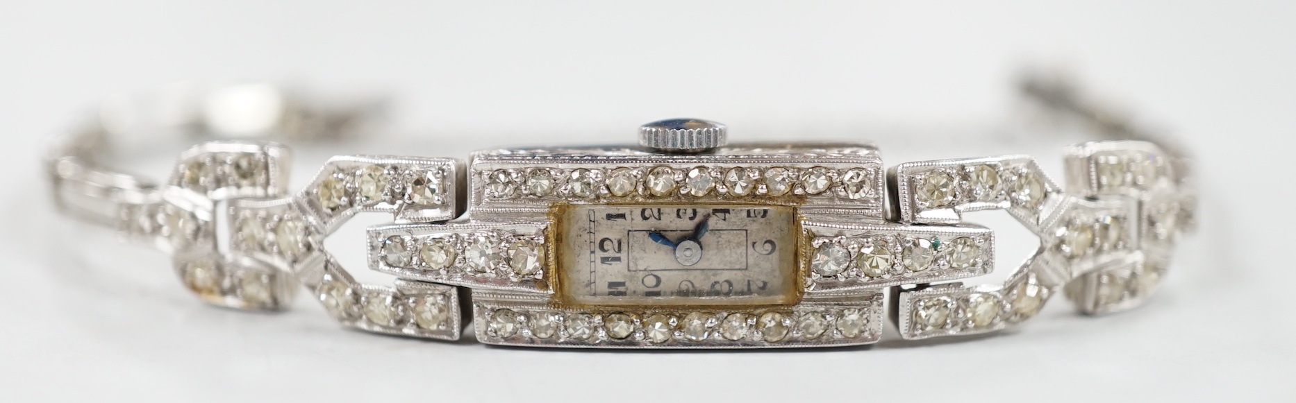 A lady's platine and diamond cluster set manual wind cocktail watch, with rectangular Arabic dial, on a white metal expanding bracelet, 16cm, gross weight 15 grams.